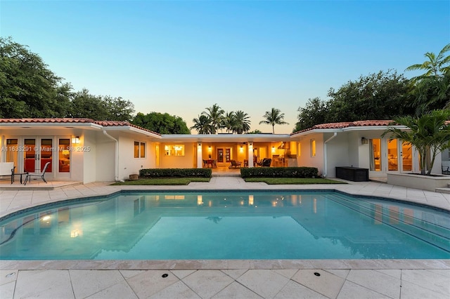 pool at dusk featuring an outdoor pool, french doors, and a patio