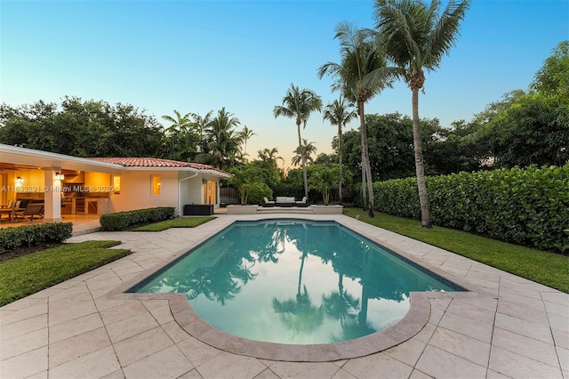 pool at dusk with fence, an outdoor pool, a patio area, and an outdoor hangout area