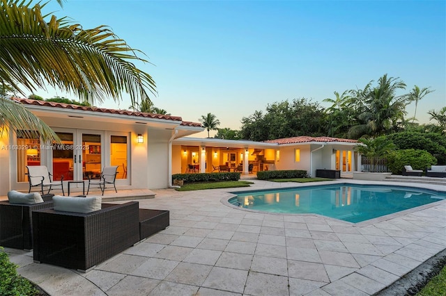 pool at dusk with french doors and a patio area