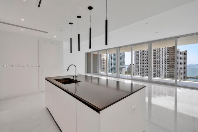 kitchen with sink, a center island with sink, white cabinets, light tile patterned floors, and hanging light fixtures