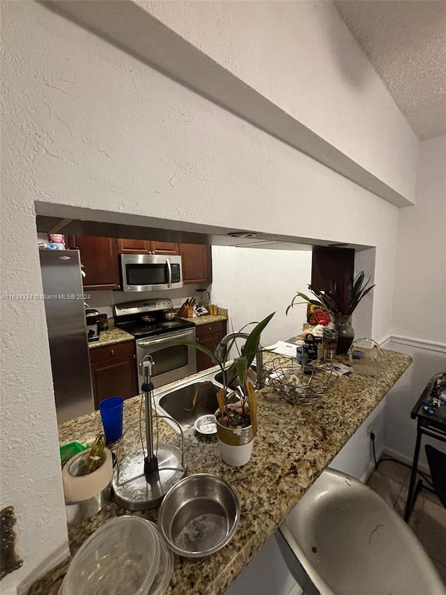 kitchen featuring sink, a textured ceiling, stainless steel appliances, and stone countertops