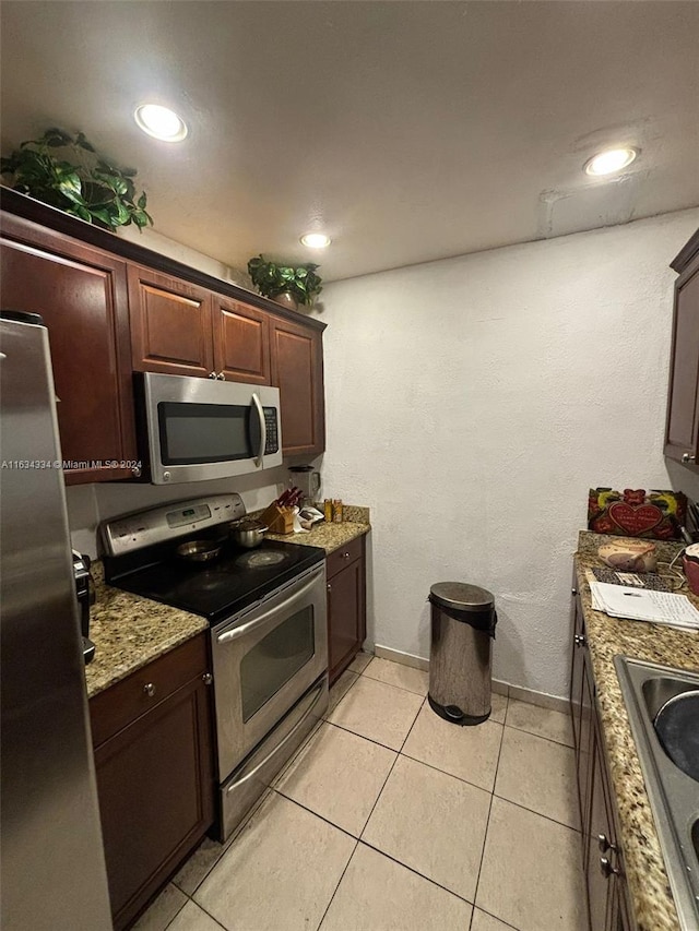 kitchen with appliances with stainless steel finishes, sink, dark brown cabinets, light stone countertops, and light tile patterned flooring