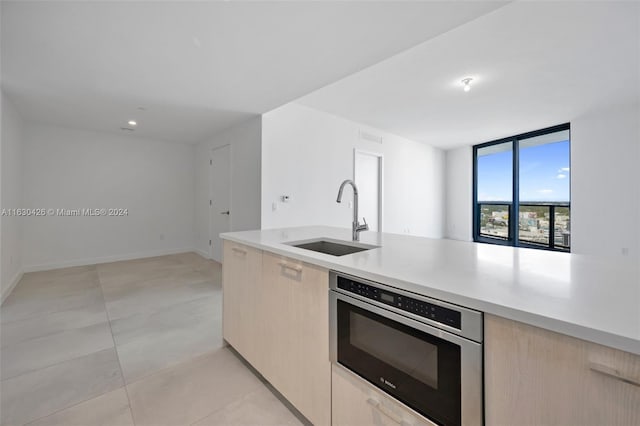 kitchen featuring sink, light brown cabinets, light tile patterned floors, expansive windows, and stainless steel oven