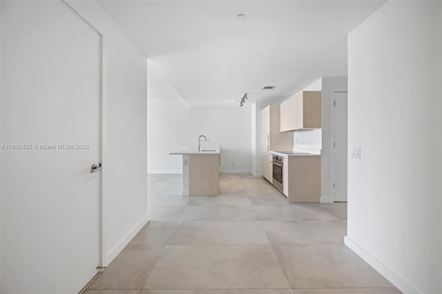 kitchen featuring light brown cabinetry, oven, sink, light tile patterned floors, and a kitchen island with sink