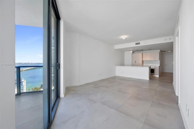 unfurnished living room featuring light tile patterned flooring, sink, a water view, and a wall of windows