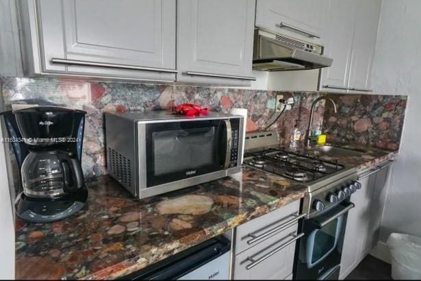 kitchen featuring appliances with stainless steel finishes, white cabinetry, dark stone countertops, and backsplash