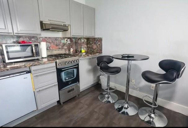 kitchen with gas range, dark hardwood / wood-style flooring, tasteful backsplash, and refrigerator