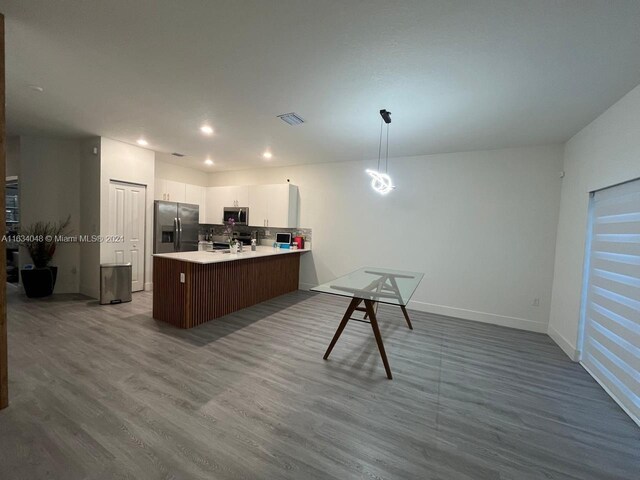 kitchen featuring stainless steel appliances, white cabinetry, tasteful backsplash, pendant lighting, and wood-type flooring