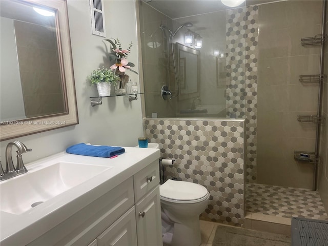 full bath featuring toilet, vanity, a tile shower, and visible vents