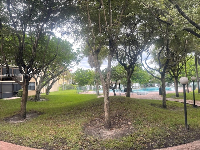 view of community with fence, a pool, and a yard