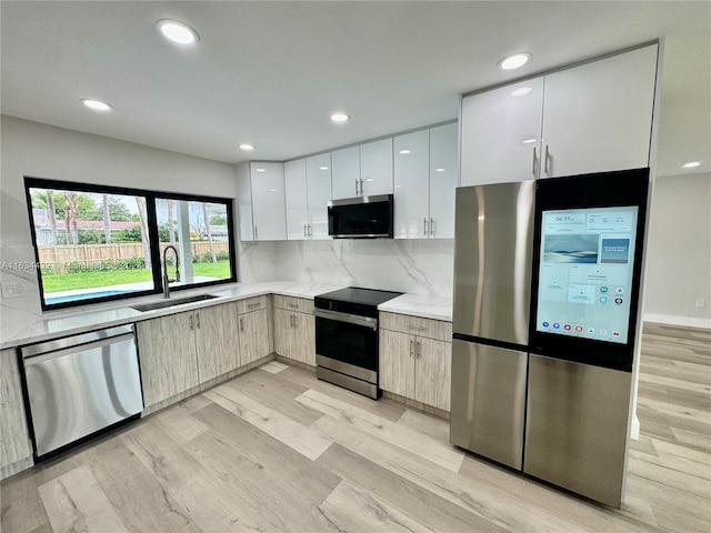 kitchen with light wood-type flooring, white cabinets, backsplash, appliances with stainless steel finishes, and sink