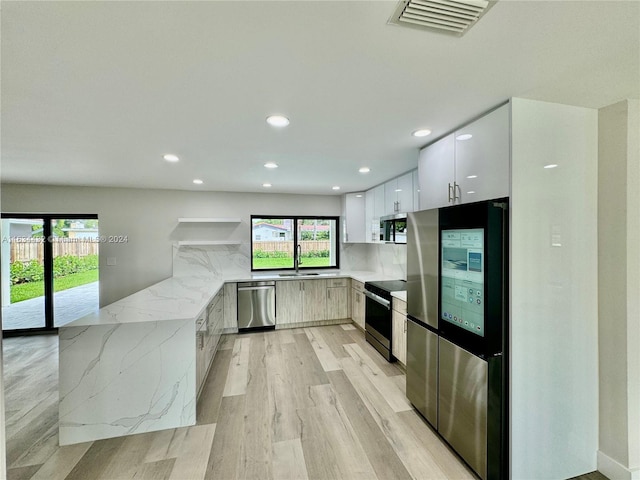 kitchen featuring appliances with stainless steel finishes, sink, light stone counters, light hardwood / wood-style floors, and white cabinetry