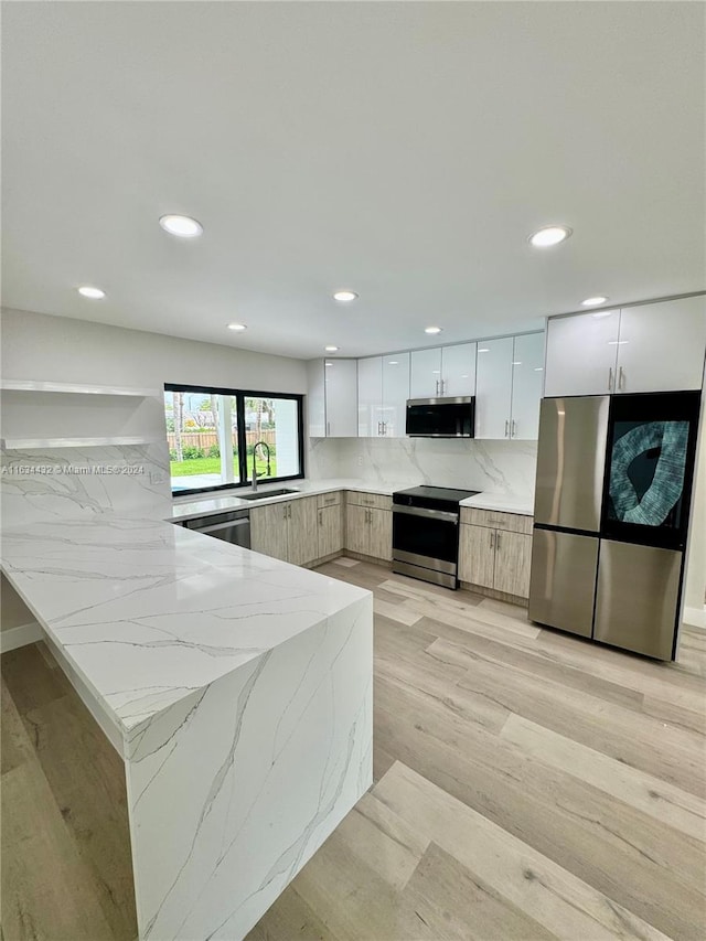 kitchen featuring tasteful backsplash, white cabinets, light stone counters, light hardwood / wood-style floors, and appliances with stainless steel finishes