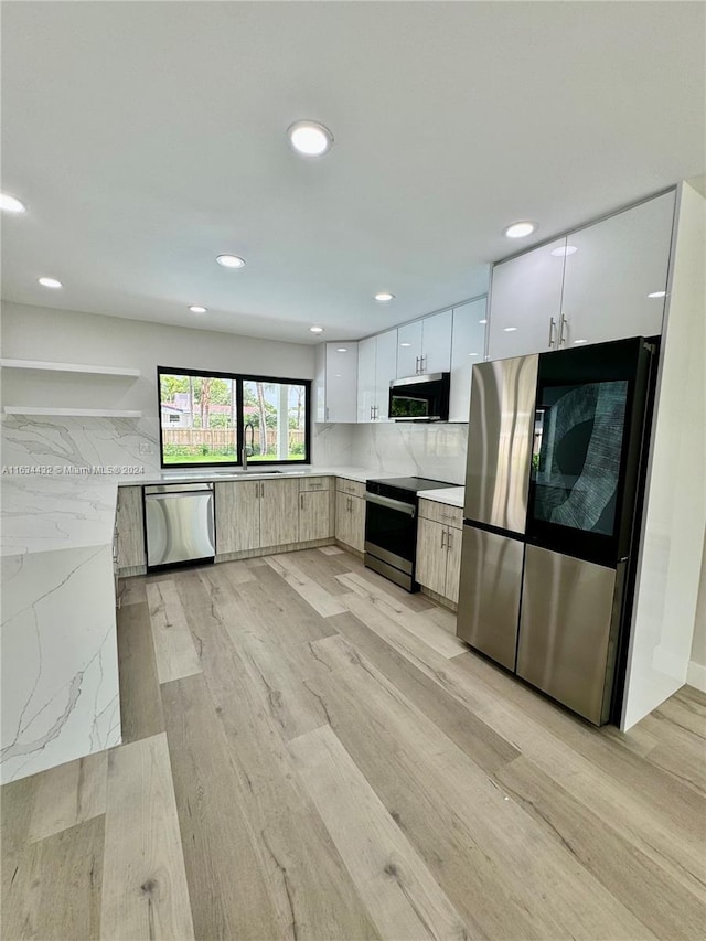 kitchen featuring white cabinetry, backsplash, appliances with stainless steel finishes, and light wood-type flooring