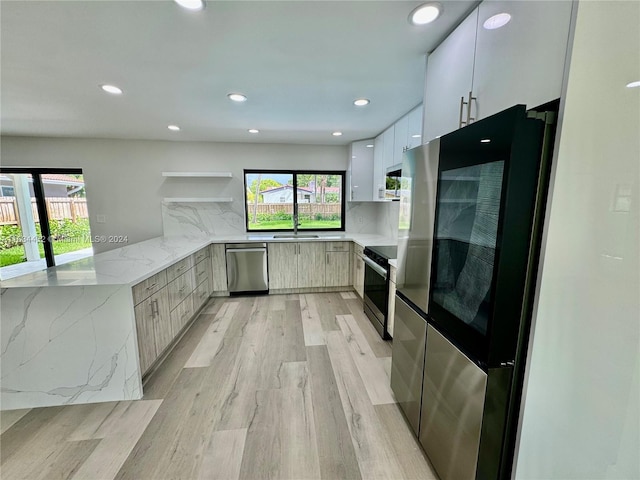 kitchen with tasteful backsplash, stainless steel appliances, white cabinets, light stone countertops, and light hardwood / wood-style floors