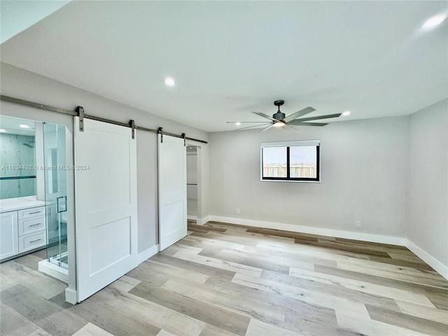 unfurnished room featuring light hardwood / wood-style floors, a barn door, and ceiling fan