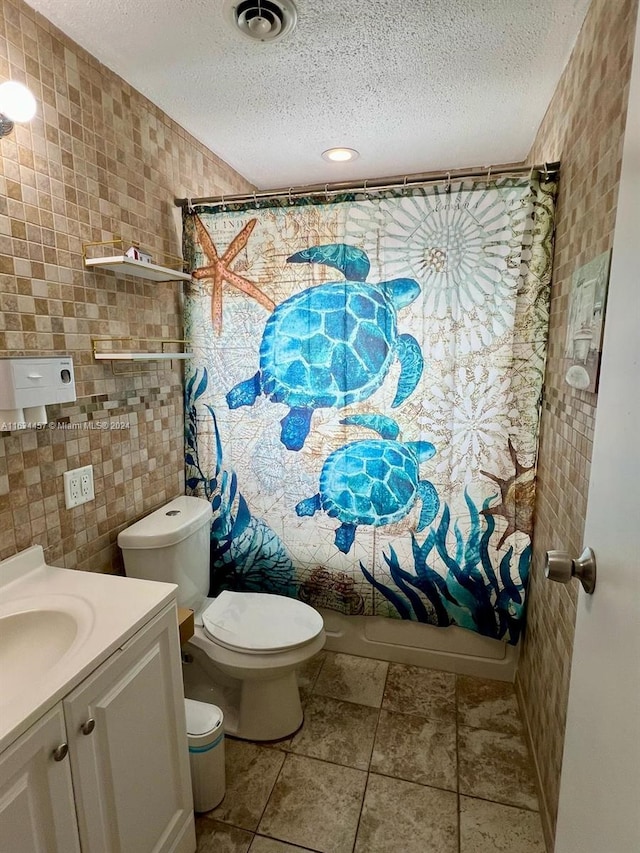 full bathroom with tile patterned flooring, a textured ceiling, shower / tub combo with curtain, vanity, and tile walls