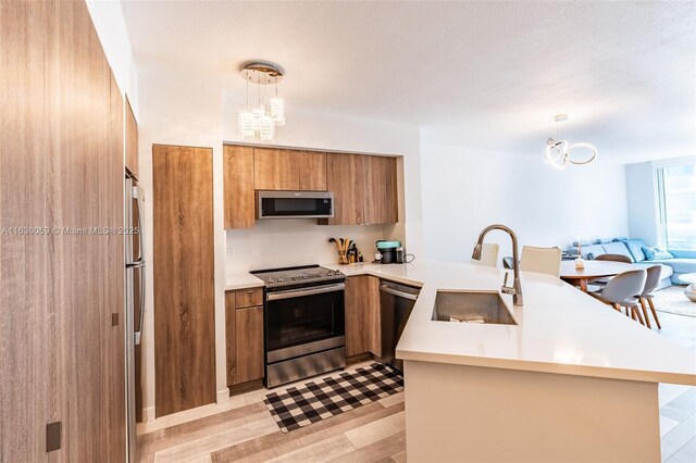 kitchen featuring kitchen peninsula, sink, decorative light fixtures, and appliances with stainless steel finishes