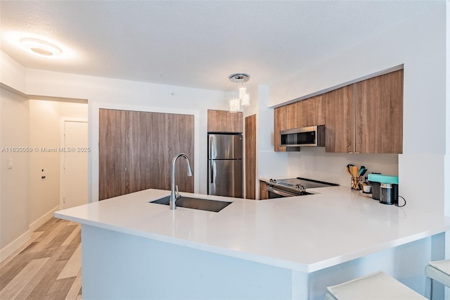 kitchen featuring sink, decorative light fixtures, light hardwood / wood-style flooring, kitchen peninsula, and stainless steel appliances