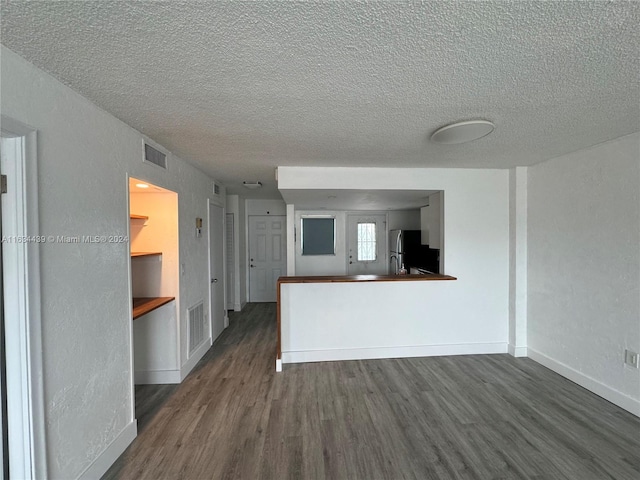 kitchen with dark wood-type flooring, fridge, kitchen peninsula, and a textured ceiling