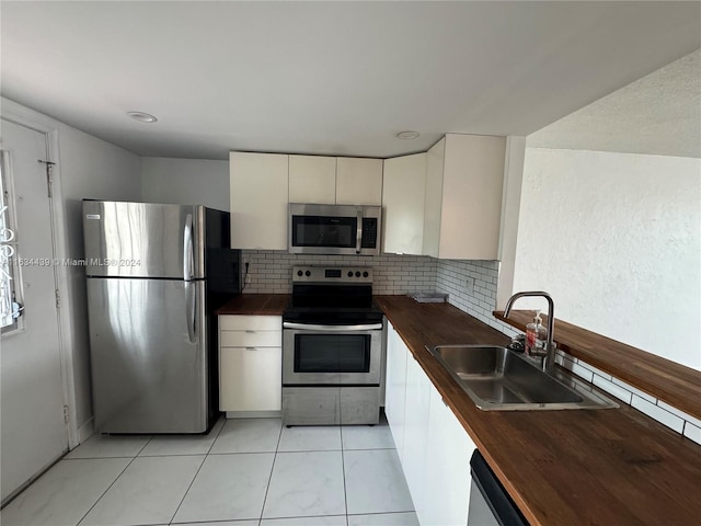 kitchen featuring butcher block countertops, stainless steel appliances, sink, light tile patterned floors, and decorative backsplash