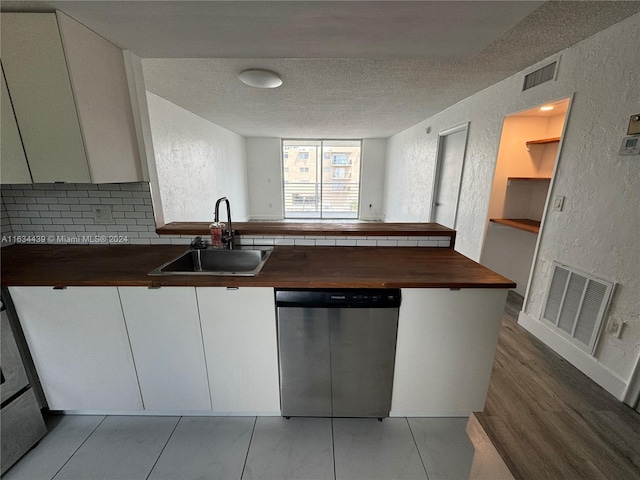 kitchen with light hardwood / wood-style flooring, a textured ceiling, wood counters, stainless steel dishwasher, and sink