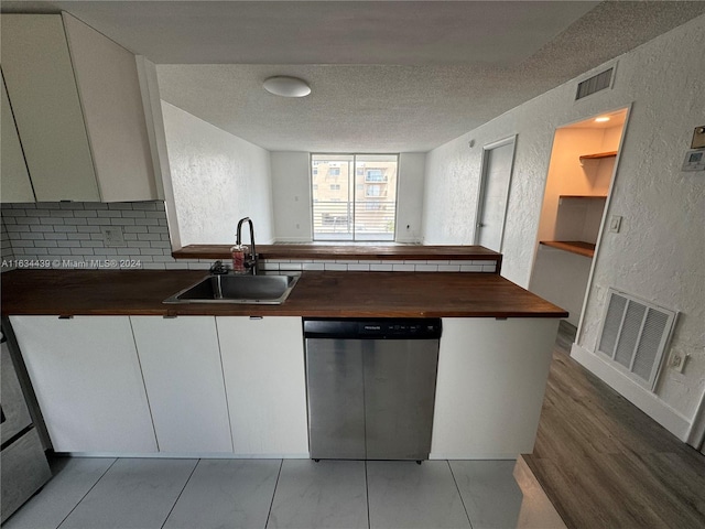 kitchen with sink, wooden counters, dishwasher, white cabinets, and a textured ceiling