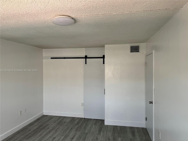 spare room featuring a textured ceiling, dark hardwood / wood-style flooring, and a barn door