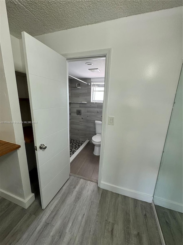 bathroom with a textured ceiling, wood-type flooring, toilet, and walk in shower