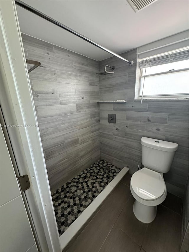 bathroom with tiled shower, tile patterned flooring, toilet, and tile walls