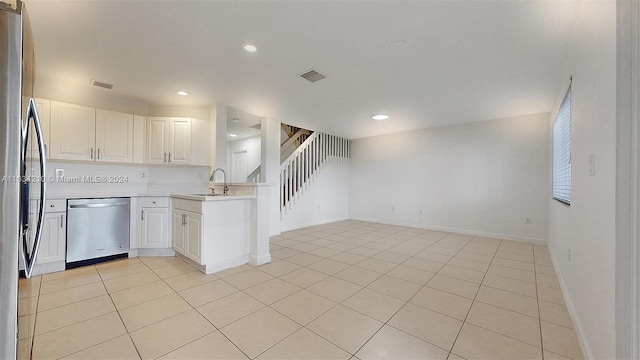 kitchen with white cabinets, stainless steel appliances, sink, kitchen peninsula, and light tile patterned floors