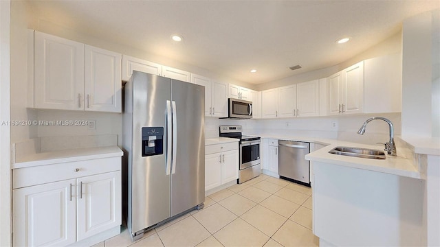 kitchen with appliances with stainless steel finishes, light tile patterned flooring, white cabinets, and sink