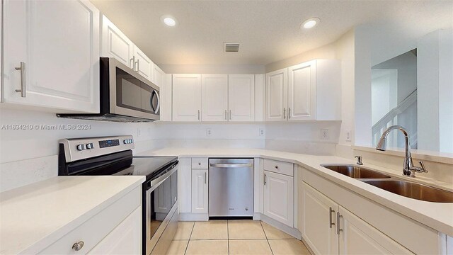 kitchen featuring appliances with stainless steel finishes, sink, a textured ceiling, light tile patterned flooring, and white cabinetry