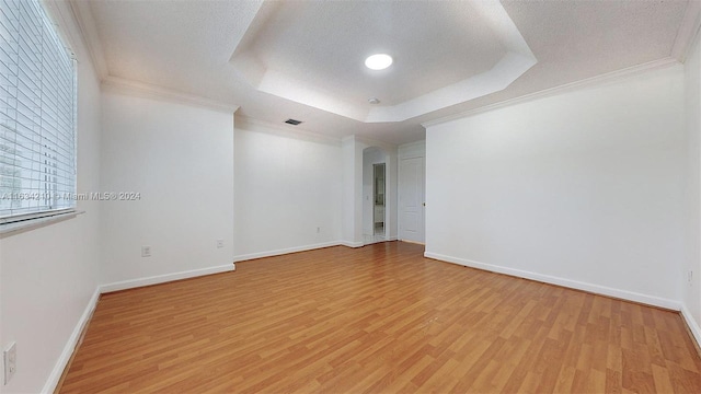 spare room featuring crown molding, a textured ceiling, a raised ceiling, and light hardwood / wood-style floors