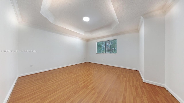 unfurnished room with ornamental molding, light hardwood / wood-style flooring, a textured ceiling, and a raised ceiling