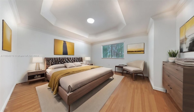 bedroom with crown molding, light hardwood / wood-style floors, and a raised ceiling