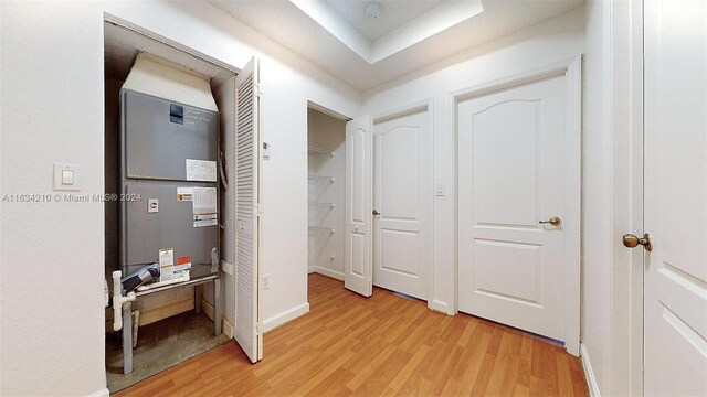 hallway featuring light wood-type flooring, heating unit, and a raised ceiling