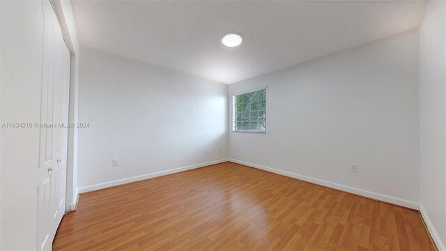 empty room with light wood-type flooring, lofted ceiling, and a textured ceiling