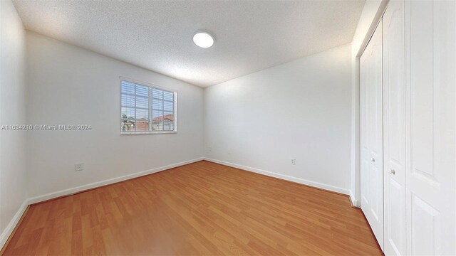 unfurnished bedroom with a textured ceiling, a closet, and wood-type flooring