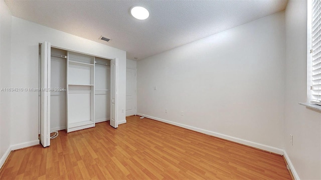 unfurnished bedroom featuring a textured ceiling, a closet, and light wood-type flooring