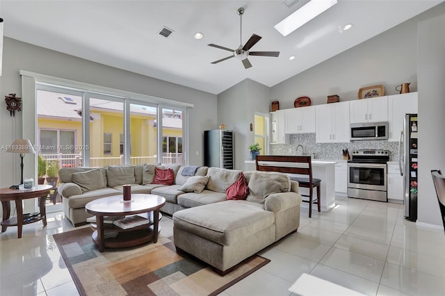 living room featuring light tile patterned flooring, high vaulted ceiling, a skylight, sink, and ceiling fan