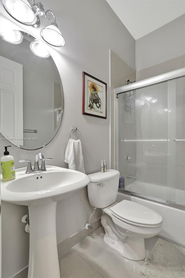 full bath with tile patterned floors, toilet, a sink, combined bath / shower with glass door, and baseboards