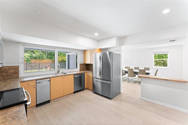 kitchen featuring appliances with stainless steel finishes, sink, light brown cabinets, decorative backsplash, and light wood-type flooring