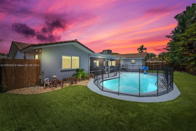 pool at dusk featuring a patio and a lawn