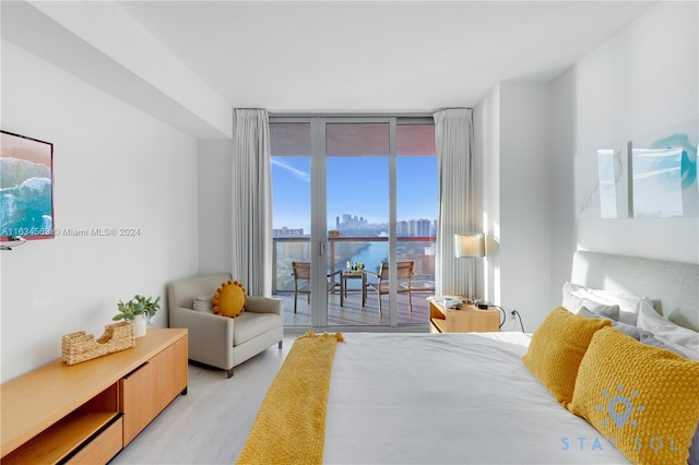 bedroom featuring a wall of windows, a water view, access to outside, and light hardwood / wood-style flooring