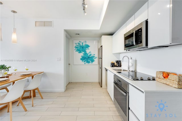 kitchen featuring stainless steel appliances, hanging light fixtures, white cabinets, light tile patterned floors, and track lighting