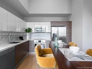 kitchen with appliances with stainless steel finishes, tasteful backsplash, white cabinets, sink, and light hardwood / wood-style floors