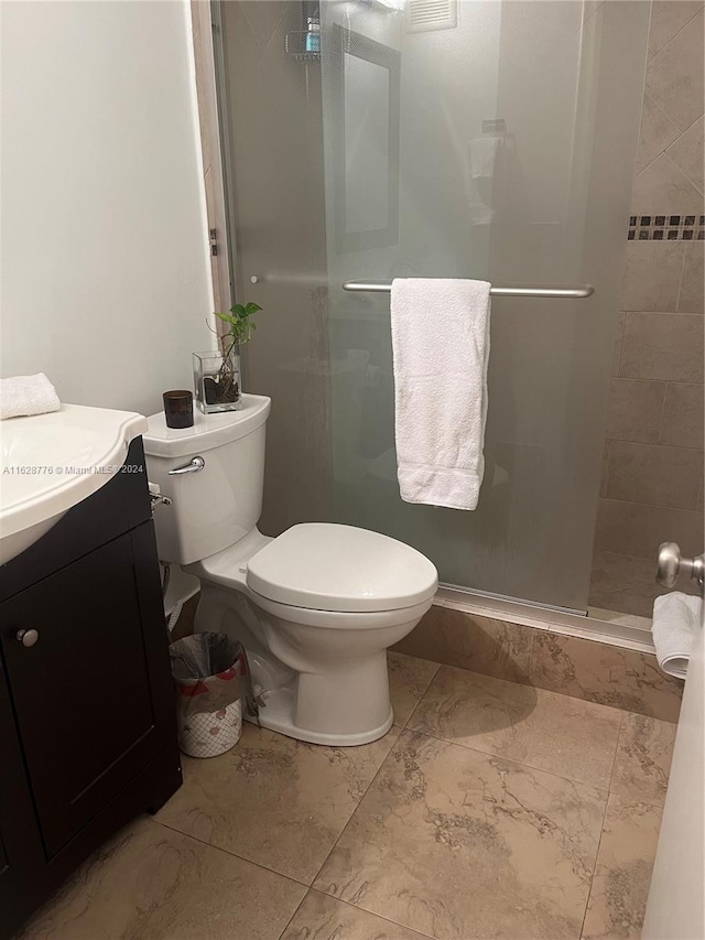 bathroom with a shower with door, vanity, tile patterned floors, and toilet