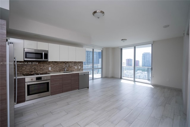 kitchen with appliances with stainless steel finishes, decorative backsplash, floor to ceiling windows, sink, and white cabinetry