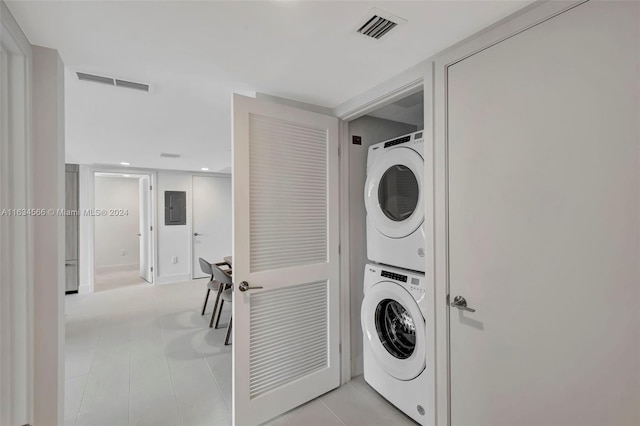 laundry area featuring light tile patterned flooring, stacked washing maching and dryer, and electric panel